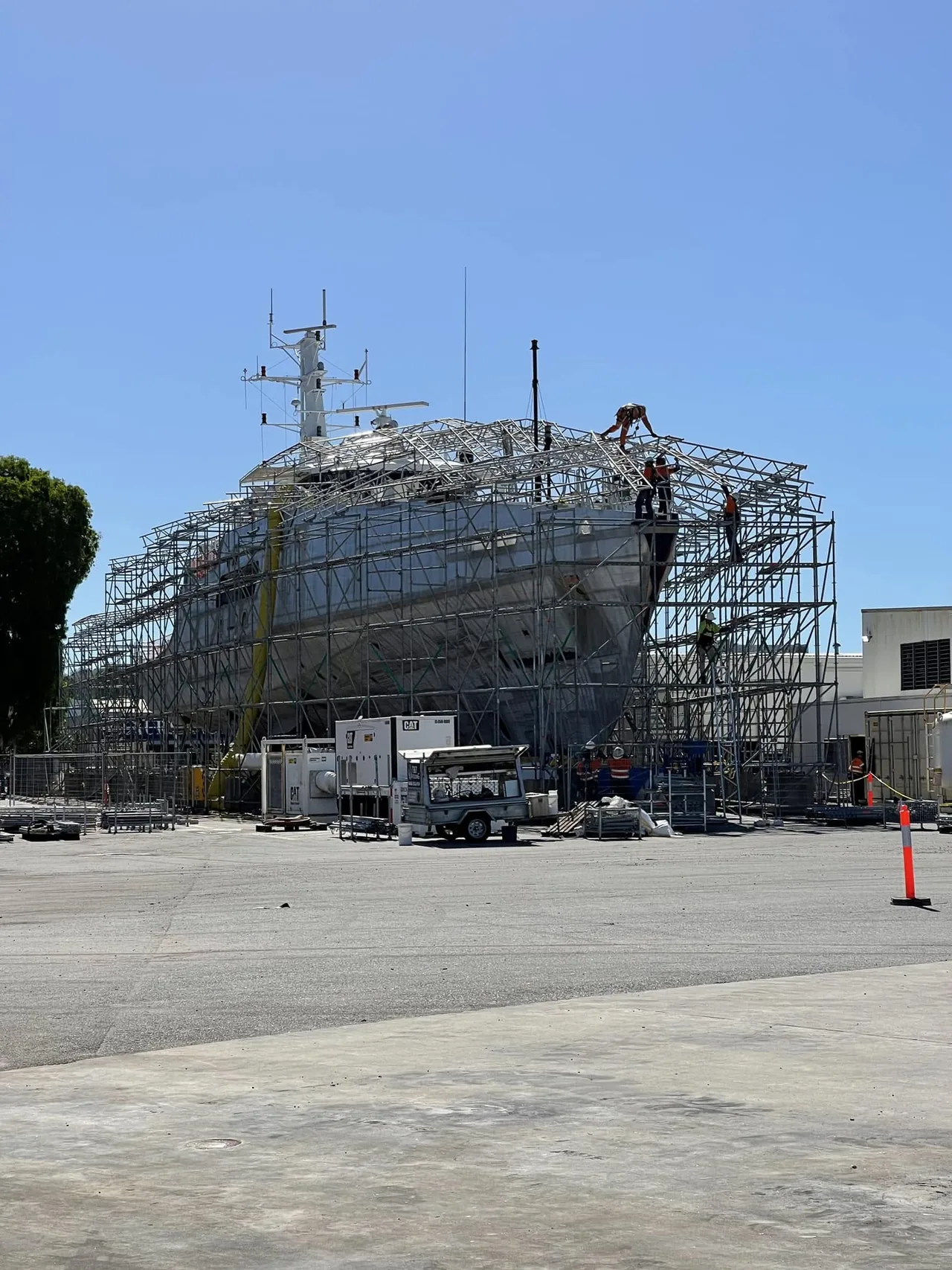 Workers assembling a roofed scaffold enclosure around a large vessel