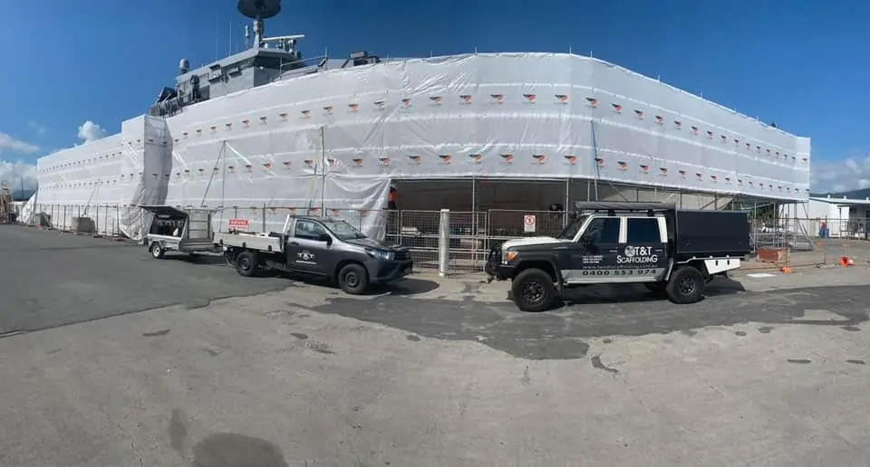 Large structure fully wrapped in white shrink wrap with T & T Scaffolding vehicles in front